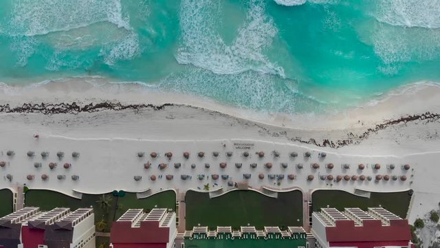 Aerial shot of tropical white sand beach in Cancun. Moving down the coast in Mexico with all inclusive resorts, beach umbrellas and beautiful blue ocean water. Looking down along coastline.