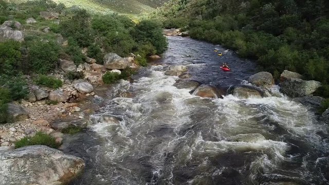 Aerial footage of white water kayaks paddling in the white water rapids on a freestone stream in the western cape of south africa during a winter storm.