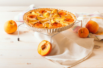 Open pie with peaches in almond cream on a white wooden background. Delicious and sweet peach tart