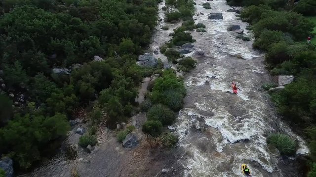 Aerial footage of white water kayaks paddling in the white water rapids on a freestone stream in the western cape of south africa during a winter storm.