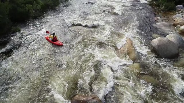 Aerial footage of white water kayaks paddling in the white water rapids on a freestone stream in the western cape of south africa during a winter storm.