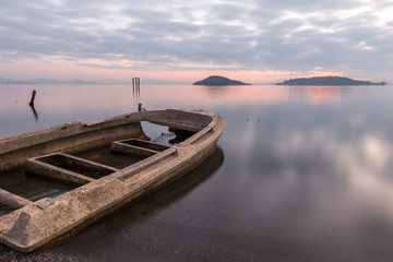 Fototapeta premium Beautiful view of Trasimeno lake (Umbria) at dusk, with a little, old boat partially filled by water, perfectly still water and a mackerel sky