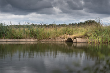 sewage from the sewer pollutes a lake or water gushing from the sewer to the river. Dark cloudy sky