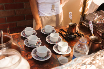 A waiter woman cooks Turkish coffee on the street in a mobile trolley and pours it over the cups.