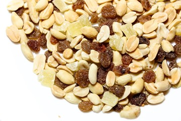 On a white isolated background lies a mixture of nuts and fruits. The mixture consists of peanuts, candied fruits, raisins and dried bananas.