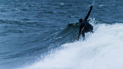 Surfer in black wet suit riding a wave in storm