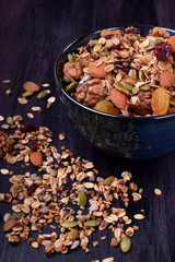 Granola made of cereals, nuts and seeds in a bowl and scattered around the dark table