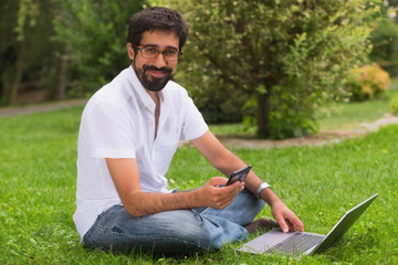 Obraz premium Young happy smiling man working with laptop and cellphone, outdoors