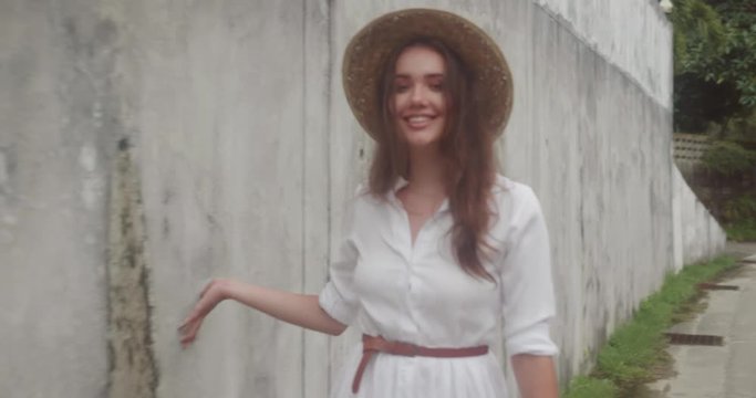 Fashion beauty portrait of smiling girl in white dress and straw hat isolated over grey concrete wall