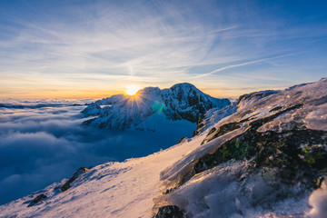 Stunning sunset or sunrise in winter alpine like snow landscape. Inversion, sun star peaking behind high rocky and icy summit. Purple, pink, blue and orange colors. Ladovy stit in winter High Tatras.