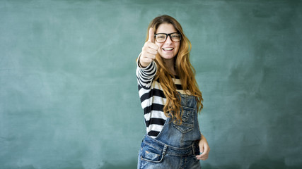 Young student girl showing thumbs up on green chalkboard