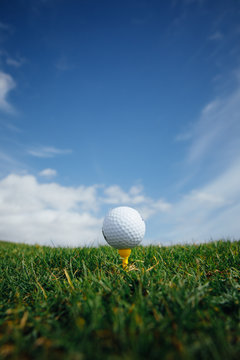 Golf Ball On Tee, Green Grass And Blue Sky Background