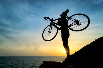 Silhouette of bicyclist carrying his bicycle on shoulder while walk against on colorful sunset orange sky background. Active outdoors lifestyle for healthy concept.