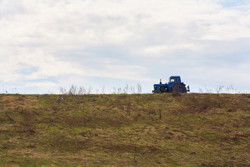 Obraz premium A blue tractor against the background of a yellow grass and sky with clouds.
