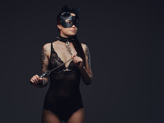 Sexy woman wearing black lingerie in BDSM cat leather mask and accessories posing on dark...