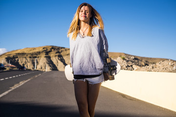 cheerful young lady walking down the street with a skateboard on his back. smile and enjoy the outdoor leisure activity and the alternative lifestyle. living under the sun concept