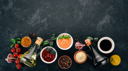 Set of sauces - Ketchup, mayonnaise, mustard, soy sauce, barbecue sauce, pepper and spices. On a black stone background. Top view. Free space for text.