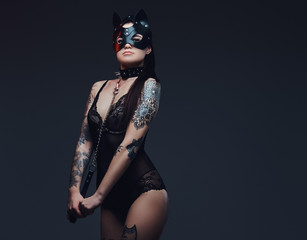 Sexy woman wearing black lingerie in BDSM cat leather mask and accessories posing on dark background. 