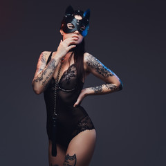 Sexy woman wearing black lingerie in BDSM cat leather mask and accessories posing on dark background. 