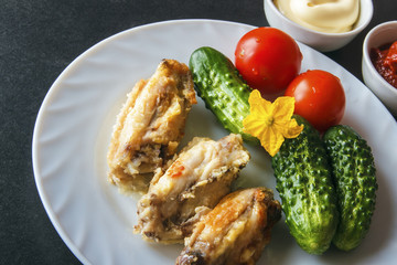 Baked chicken wings in tomato paste and mayonnaise on a white plate with fresh organic vegetables on a black background. Copy space