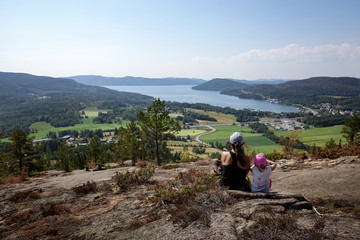 Fototapeta na wymiar Family travel. Mother and daughter rest from hiking uphill a mountain. Beautiful view of archipelago, mountains, forest and sea. Skule mountain, high coast in northern Sweden.