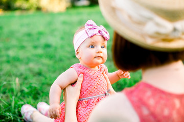 A happy family having a picnic in the green garden in a sunny spring day: a beautiful smiling mother sitting on green grass and her little laughing daughter on her legs