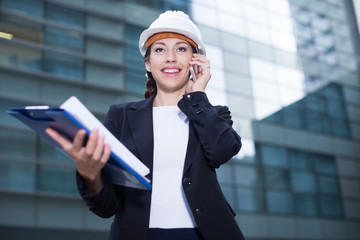 Woman architector in suit and hat is talking about project by the phone
