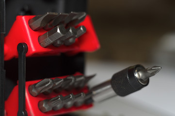 Bits holder in box and many tool bits on white background. Close-up view. Red element in plastic box.