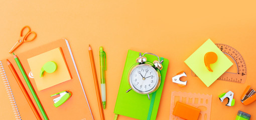 Back to school styled scene with orange and green school supplies on orange background banner