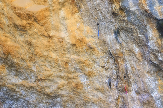 Natural climbing wall at the hillside of a rocky mountain. Carabiners ready to be used by the climbers. Soft background. Shaded spot area near to a cave.