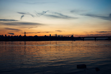 Fototapeta na wymiar Skyline, Kiev city in the evening. The right bank at sunset across the Dnieper River. Silhouette of a city on a sunset background.