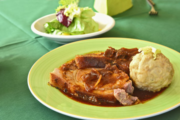 Roast pork with bread dumplings (German name is Schweinebraten mit Semmelknödel) in green dish and Green salad