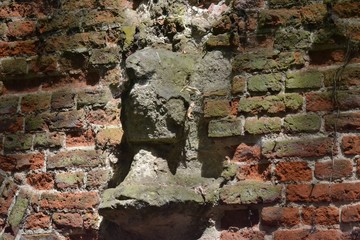 Closeup photograph of an old and weathered brick wall comprising a crumbling protrusion. The photograph was taken on a bright summer day and direct sunlight casts strong shadows.