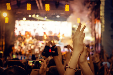 Audience with hands raised at a music festival and lights streaming down from above the stage.