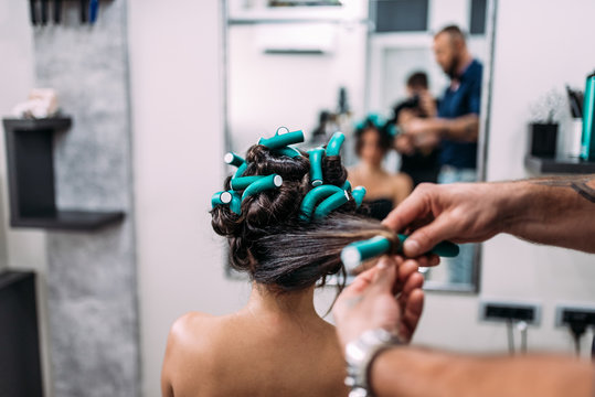 Hairdresser making hairstyle with hair curlers to a female client.