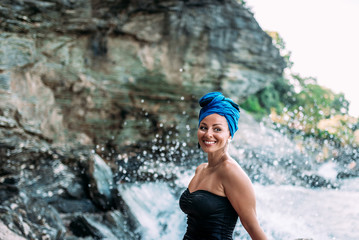 Gorgeous woman with real smile sitting in front of the water splashes on rocky sea shore.