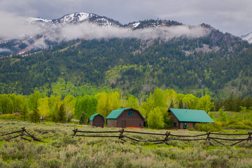 Fototapeta na wymiar Beautiful outdoor view of wooden brown houses with green roof located in lamar valley in Yellowstone National Park, Wyoming with a mountain behind, partial covered with snow