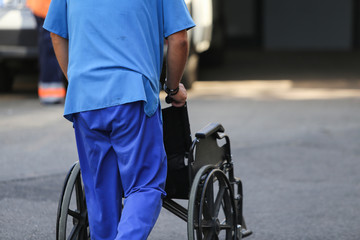 Obraz premium Man nurse pushing an empty wheelchair