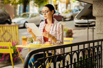 Many meals. Calm attentive woman looking at the menu and getting ready to eat her delicious dessert in a cafe