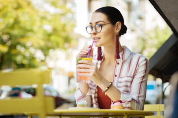 Cold lemonade. Beautiful relaxed person visiting a street cafe and using a sipping straw while drinking cold lemonade