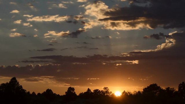Time lapse video of the sun setting with rays of light moving through the broken clouds