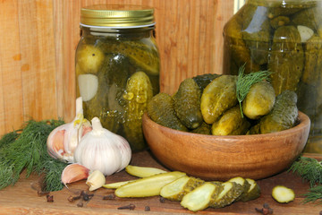 Cucumbers in a wooden bowl, fresh herbs, pickling spices and jars of pickled cucumbers on the table