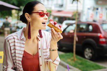 Taking a bite. Happy stylish young woman opening her mouth and biting a delicious fruit eclair...