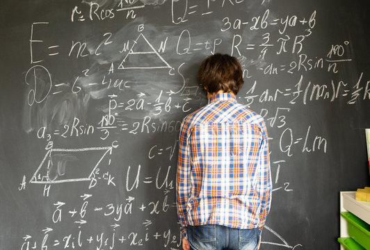 boy standing near blackboard with math formulas, school problems and neurological disorder concept