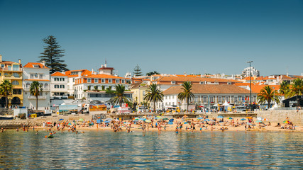Crowded sandy beach in Cascais near Lisbon, Portugal during the summer. This beach is known as Praia da Ribeira - obrazy, fototapety, plakaty