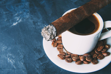 Cup of coffee, coffee beans, ashtray with cigar on dark background.