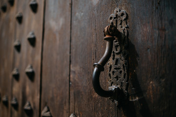 An ancient metal door knocker on the old wooden door with metal rivets in Spain