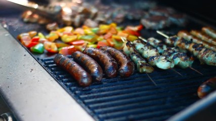 Man cooking on bbq full of food, peppers, sausages. Day time medium shot.