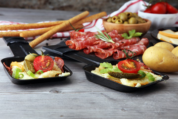 Delicious traditional Swiss melted raclette cheese on diced boiled or baked potato served in individual skillets with salami..