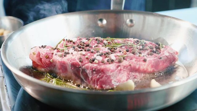 Meat steak with seasonings and herbs hissing on frying pan, close-up